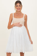 woman wearing a beige ribbed maternity dress with a white embroidered skirt and holding her baby bump
