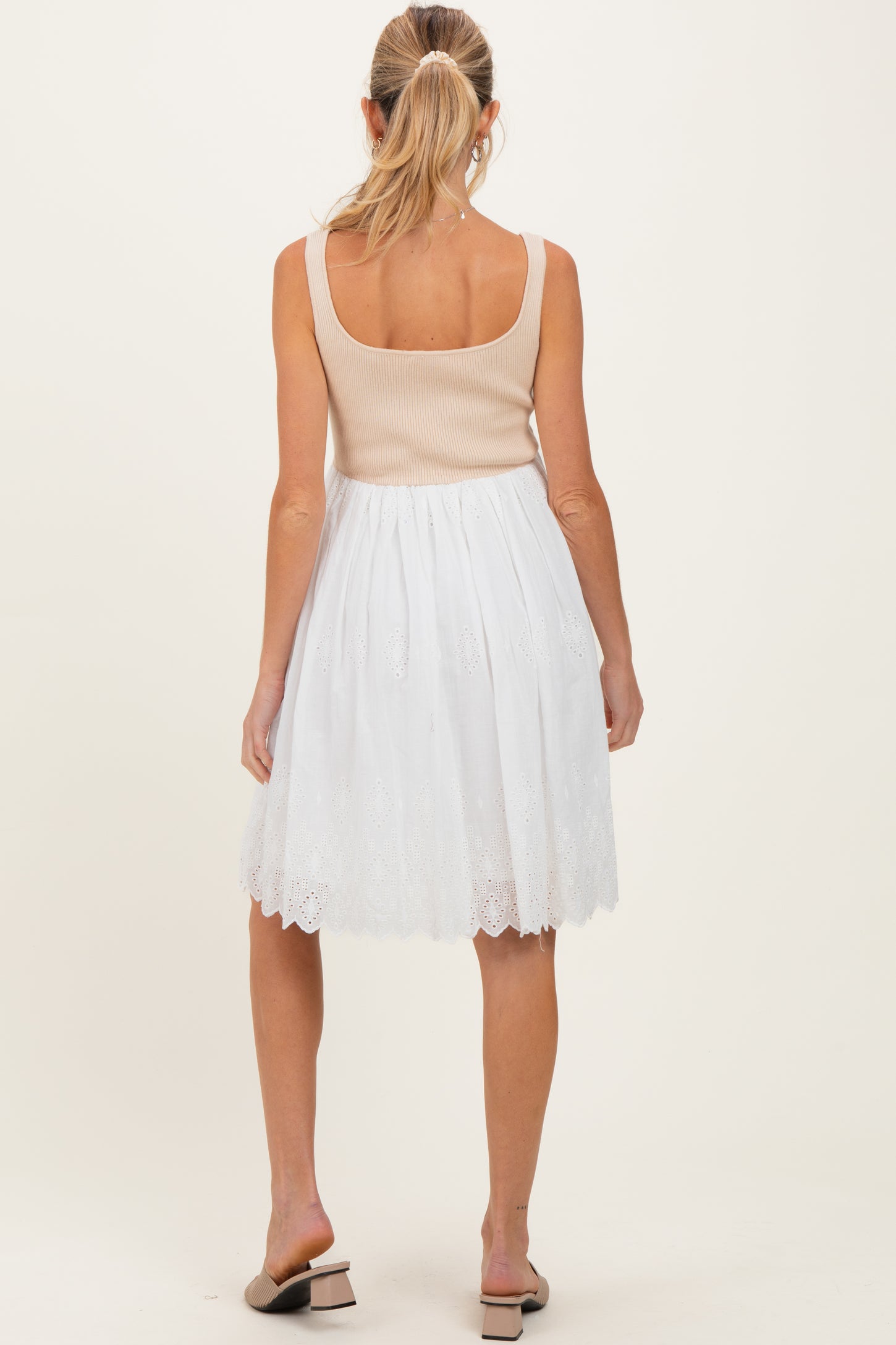 woman wearing a beige tank top and a white eyelet maternity skirt, showing a flowing style from the back