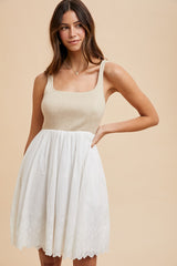 woman wearing a beige knit top and a white embroidered skirt dress with a flared silhouette