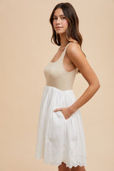 woman wearing a beige knitted bodice dress with a white eyelet skirt and side pockets