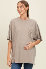 woman wearing a taupe oversized maternity t-shirt with lace pocket, gently cradling her baby bump