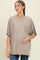woman wearing a taupe oversized maternity t-shirt with lace pocket, gently cradling her baby bump