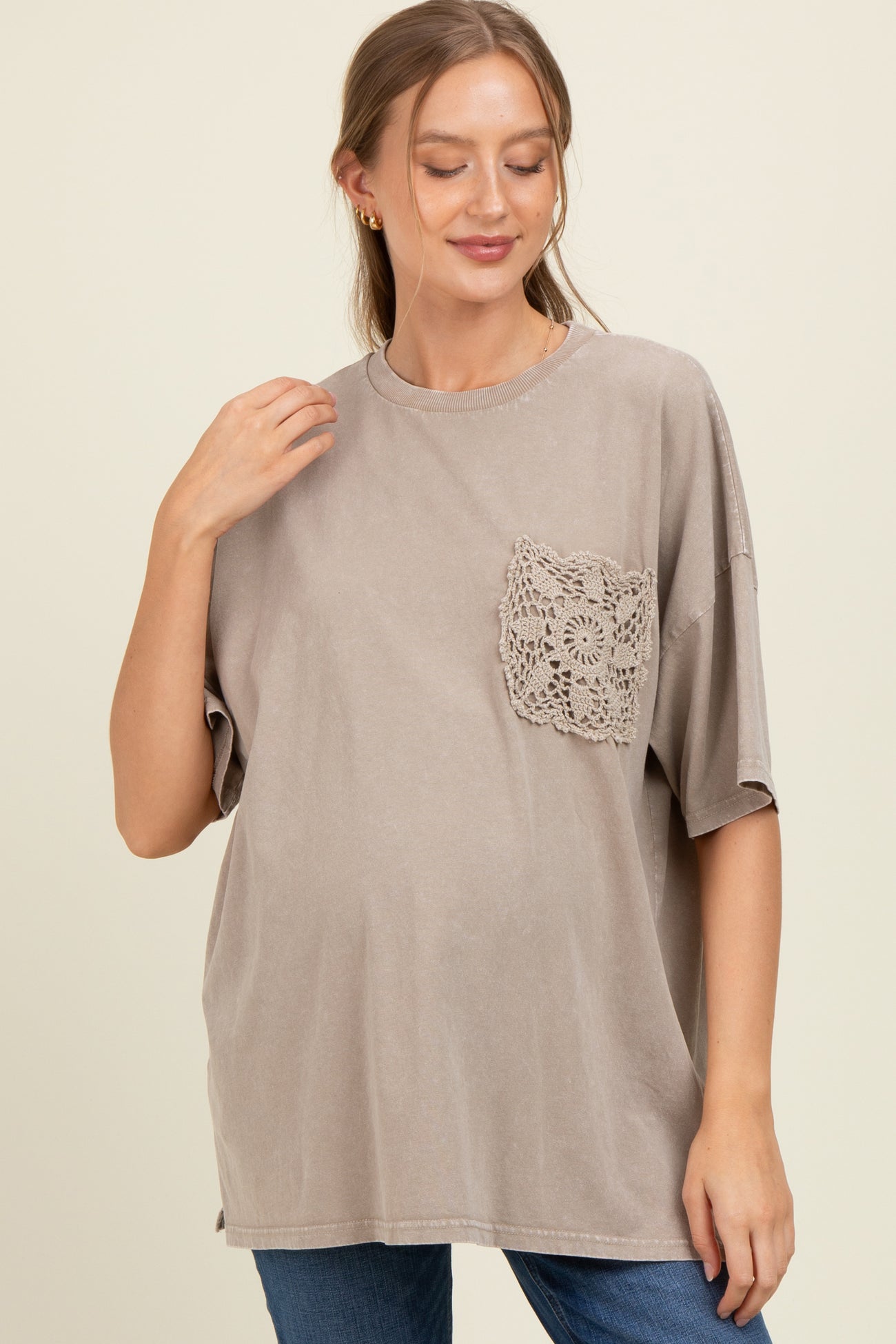 woman wearing a taupe maternity top with a lace pocket detail and a visible baby bump