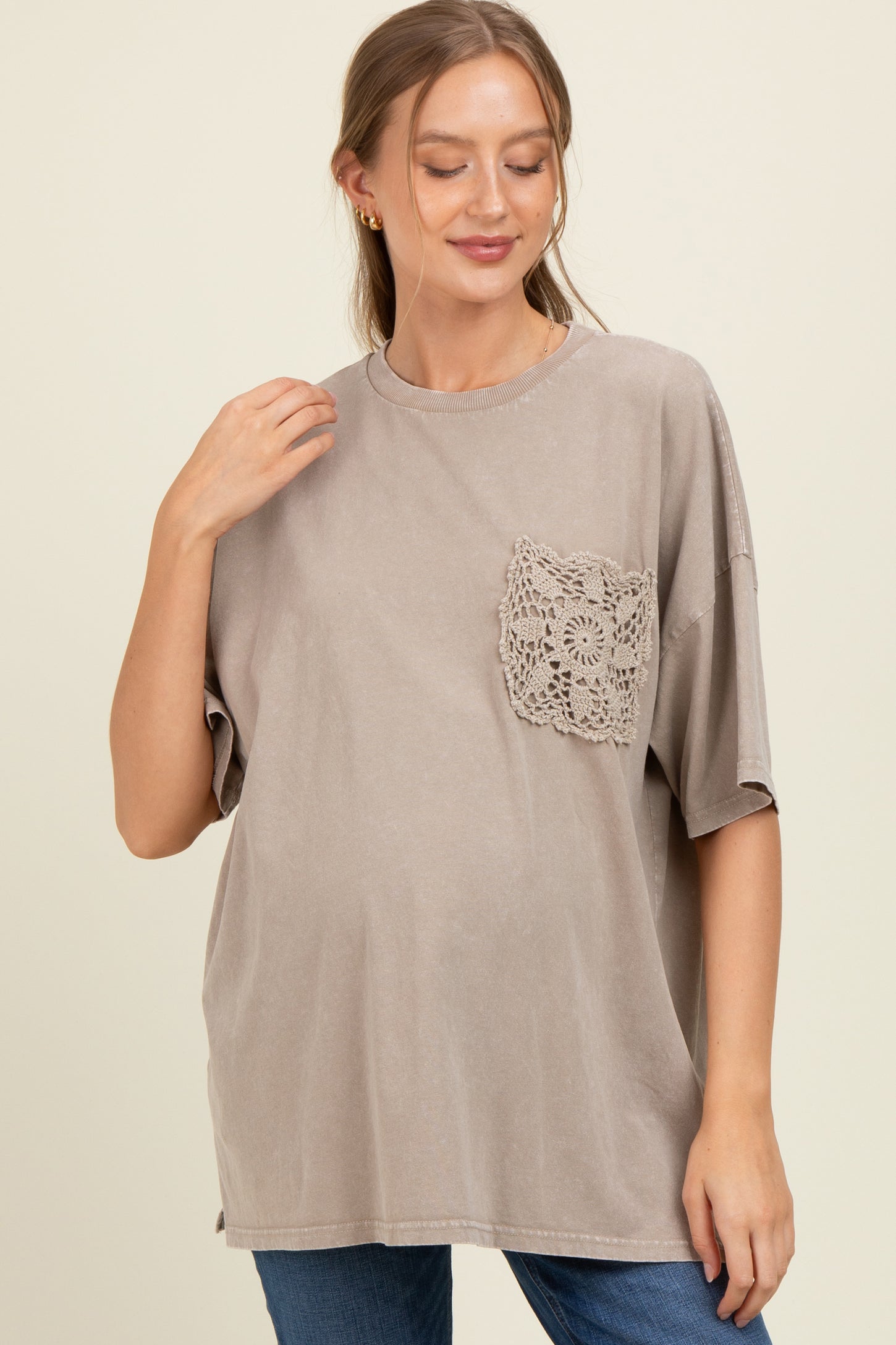 woman wearing a taupe maternity top with a lace pocket detail and a visible baby bump