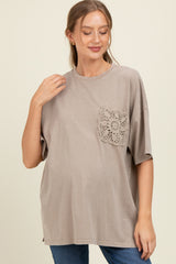 woman wearing a taupe maternity top with a lace pocket detail and a visible baby bump