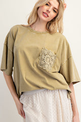 woman wearing an olive green oversized t-shirt with a crochet pocket detail and a flowy polka dot skirt