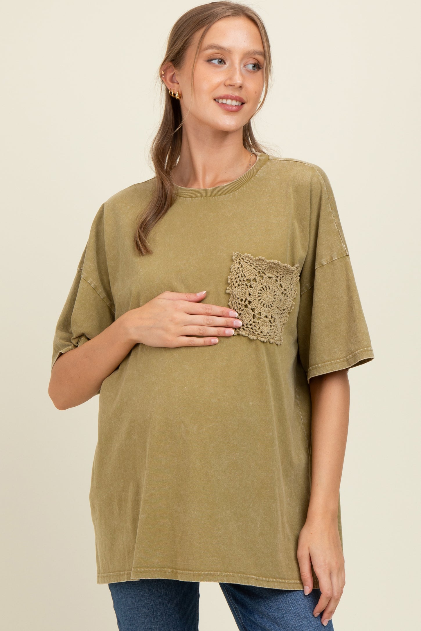 woman wearing an olive green oversized maternity tee with a lace pocket and gently holding her baby bump