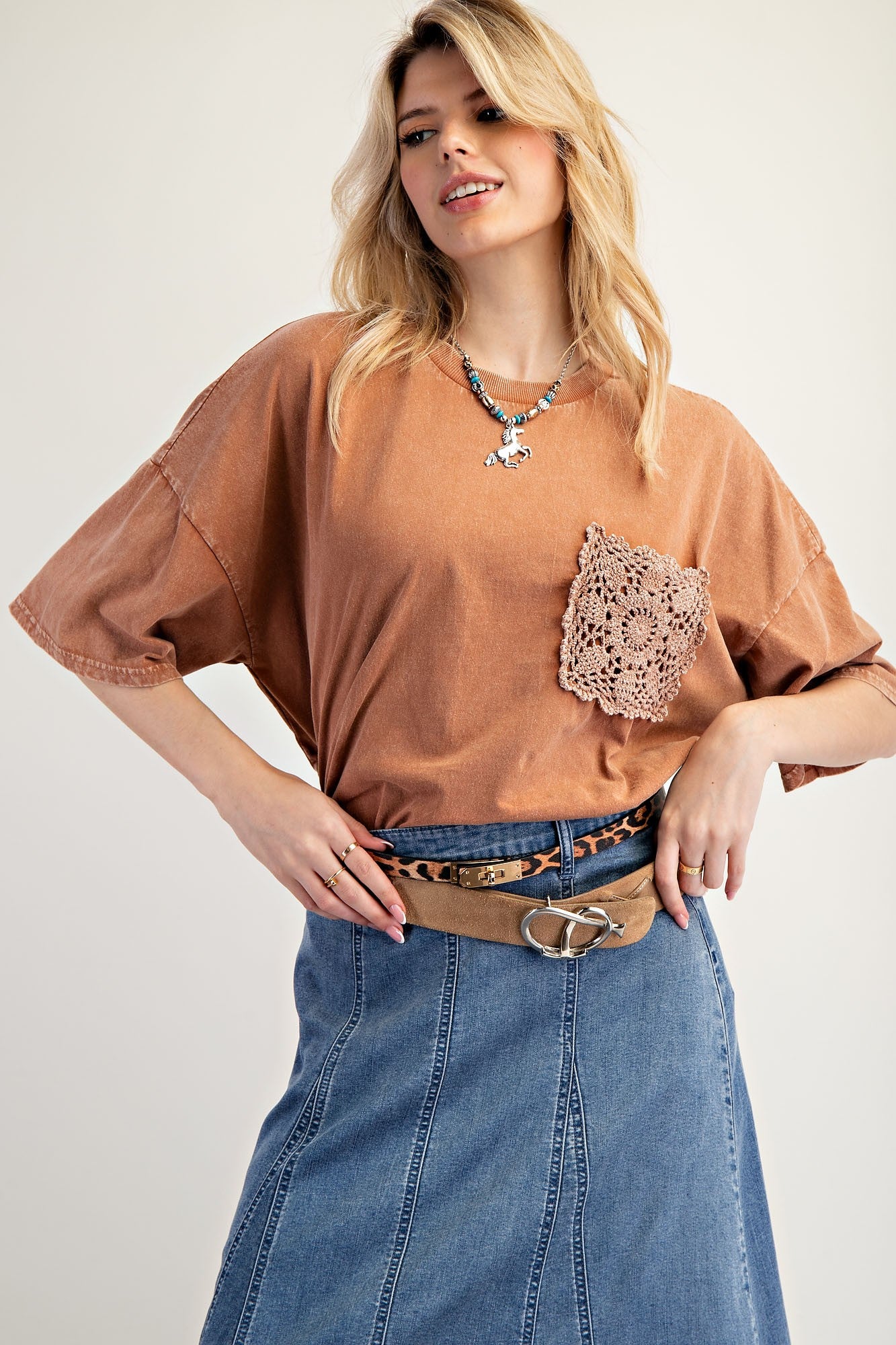 woman wearing a rust-colored oversized t-shirt with a crochet pocket and a denim skirt, smiling at the camera