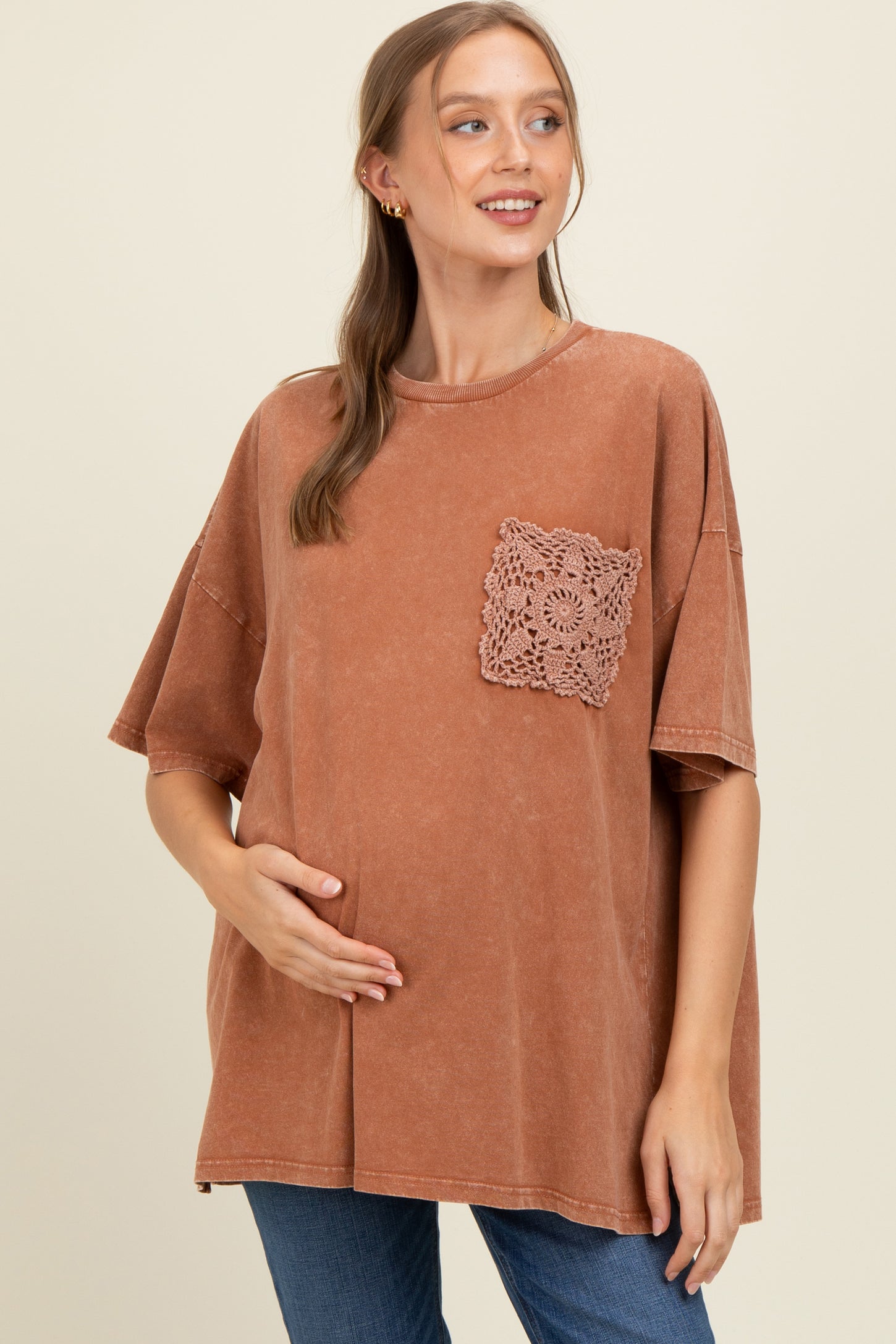 woman wearing a rust-colored oversized maternity t-shirt with a crochet pocket and gently cradling her baby bump