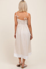 woman wearing a beige maternity dress with adjustable straps and a flowy bottom, showing off her baby bump from the back