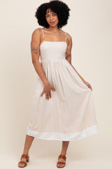 woman wearing a beige midi dress with spaghetti straps and a white hem, posing with one hand on her hip