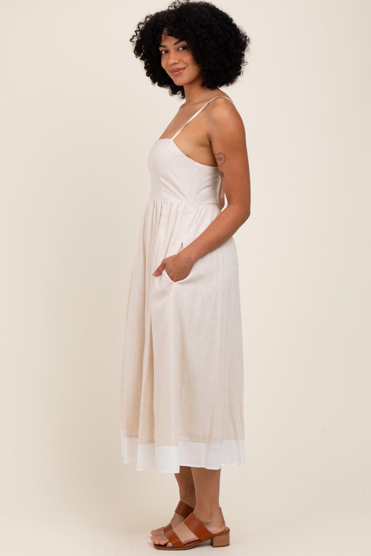 woman wearing a light beige spaghetti strap midi dress with pockets and a white hemline