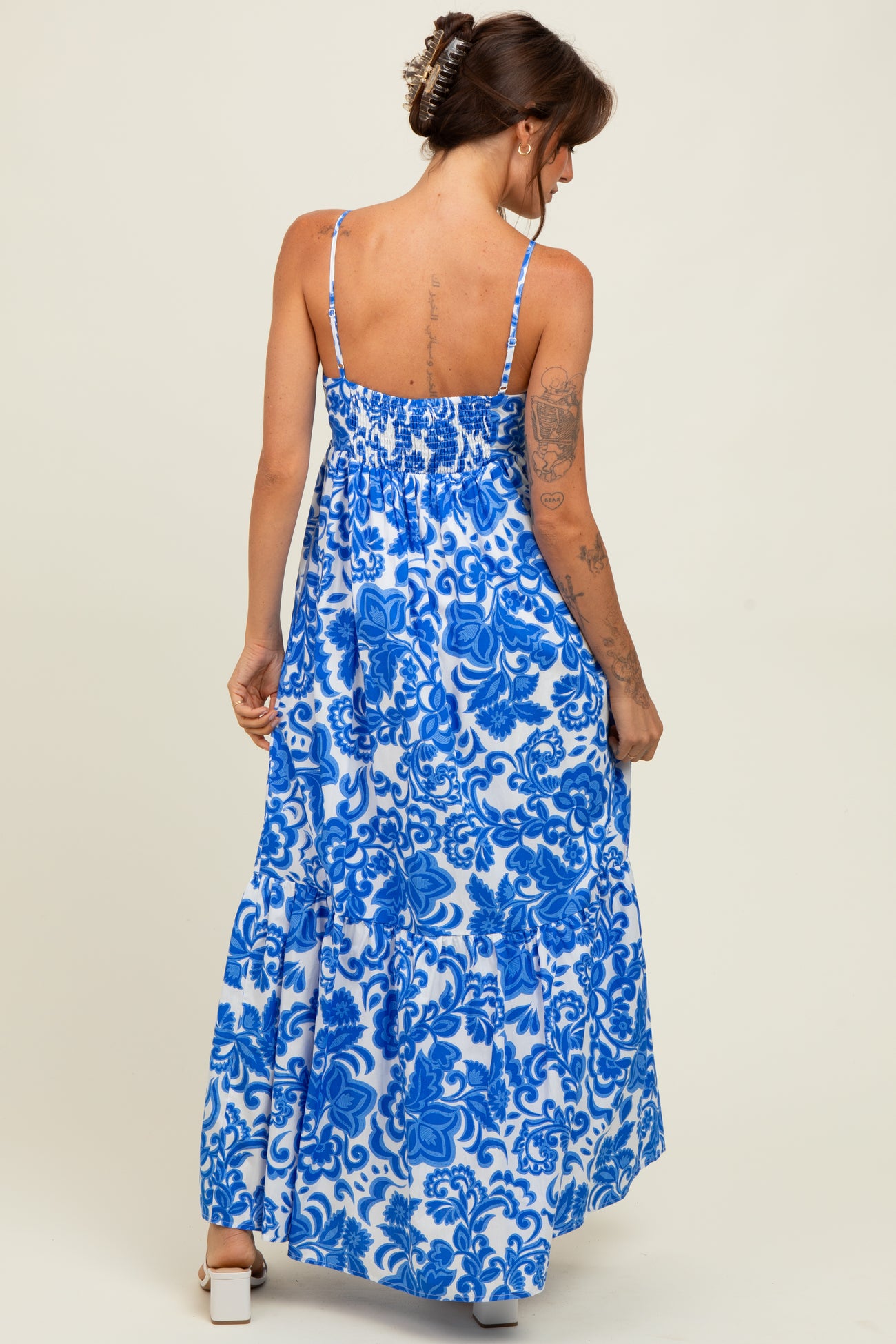 woman wearing a blue and white floral print maxi dress with thin straps and a tiered skirt, viewed from the back