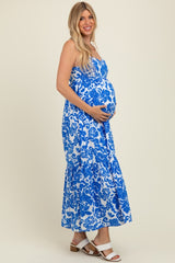 woman wearing a blue and white floral maternity maxi dress, showing her baby bump with a smile