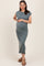 woman wearing a slate green maternity dress with cap sleeves and a baby bump, standing with one hand on her belly