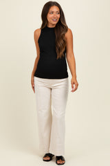 woman wearing a black maternity tank top and cream wide-leg jeans, showing her baby bump