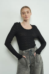 woman wearing a black long sleeve top with a scoop neckline and textured fabric, paired with gray high-waisted pants