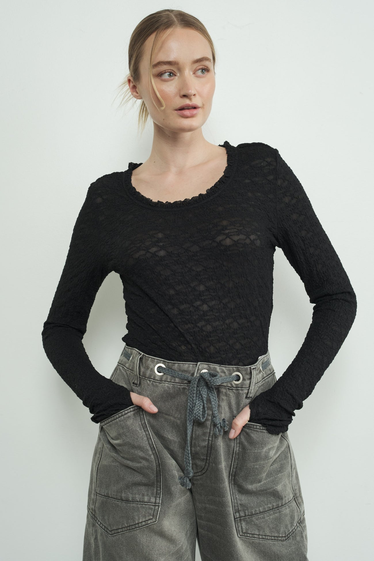 woman wearing a black lace long sleeve top with a scoop neckline and paired with gray drawstring cargo pants