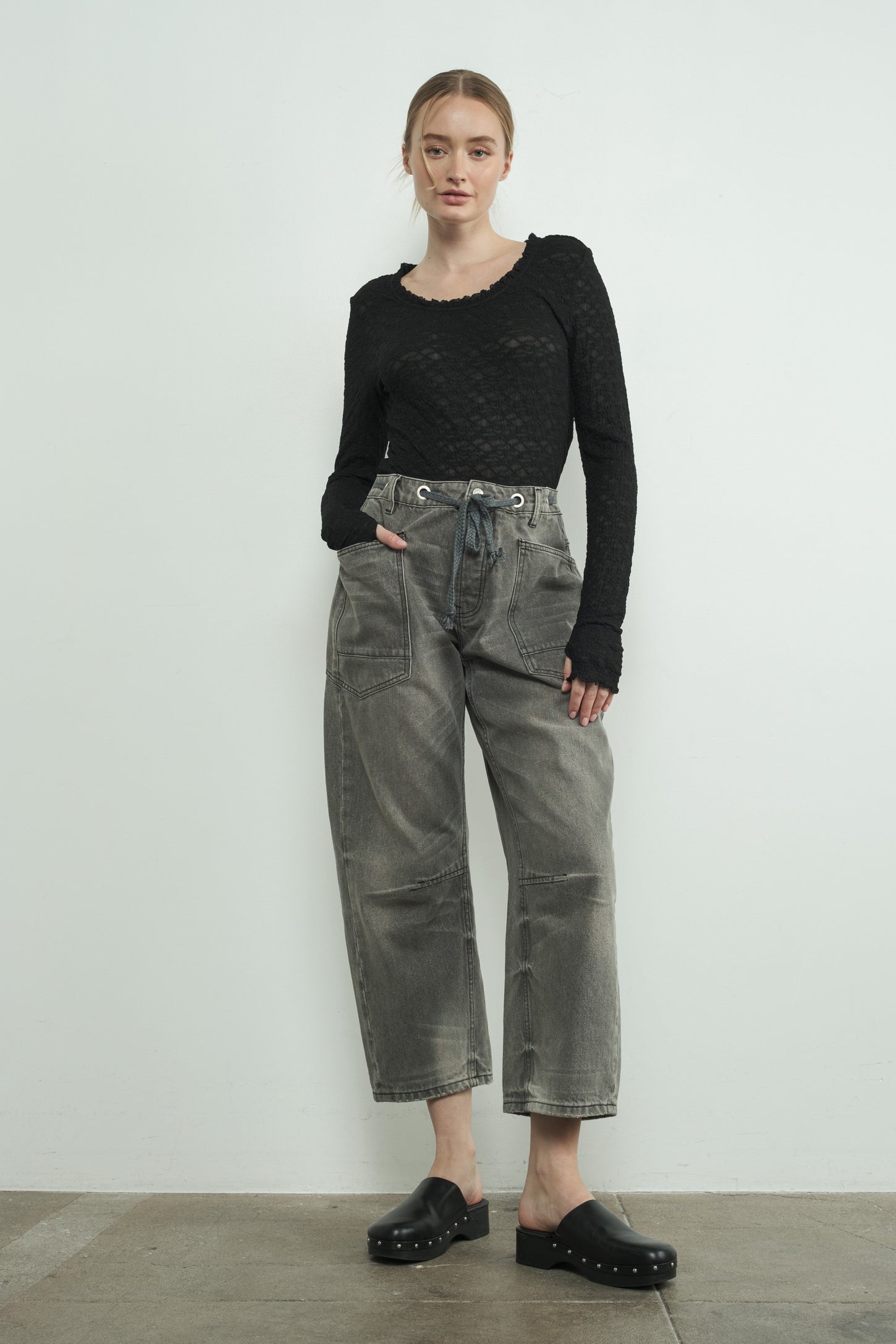 woman wearing a black long sleeve textured top and loose gray high-waisted pants with a tie belt