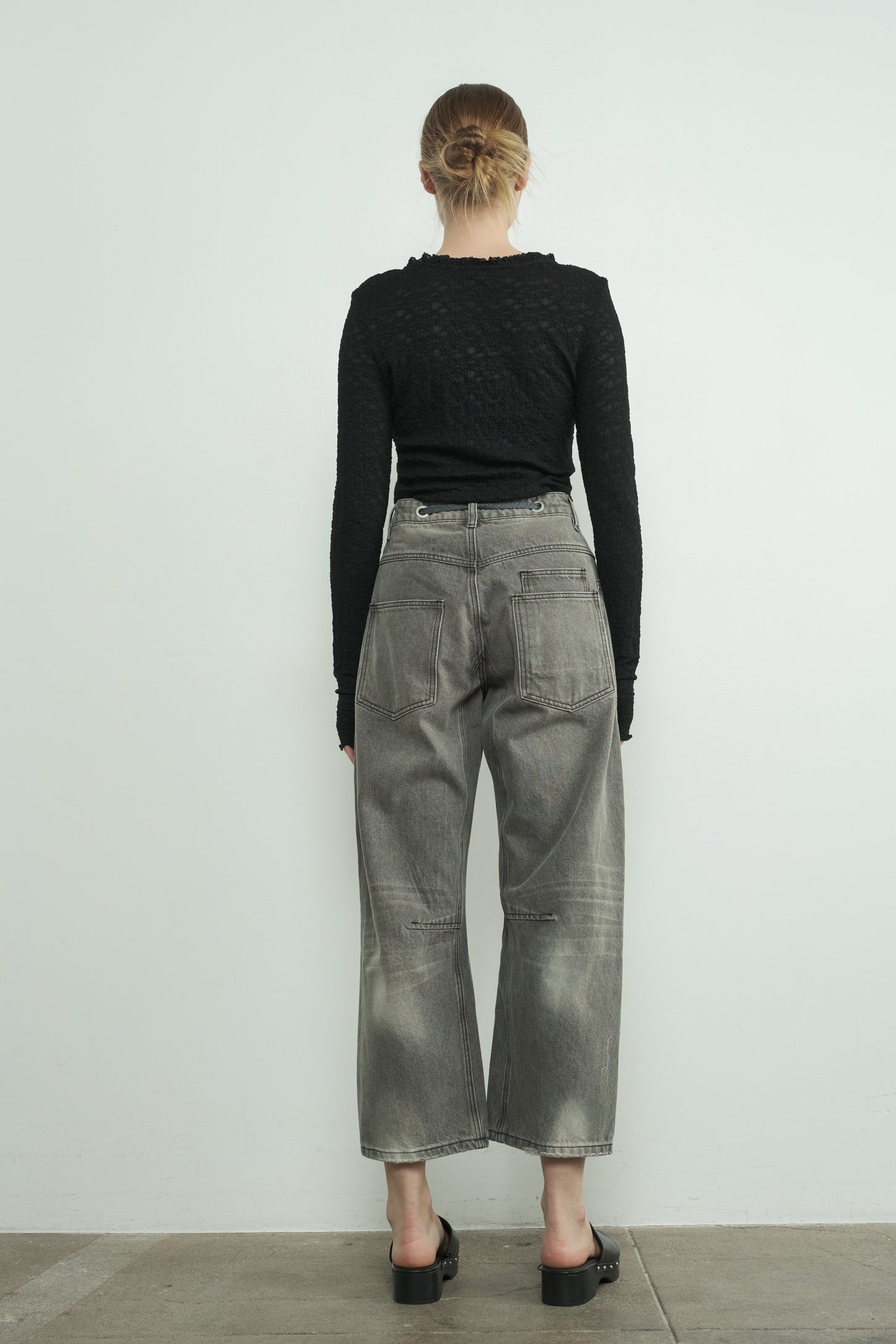 woman wearing a black textured long sleeve top and gray wide leg jeans, seen from the back