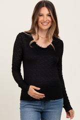 woman wearing a black long sleeve maternity top with ruffled neckline and holding her baby bump