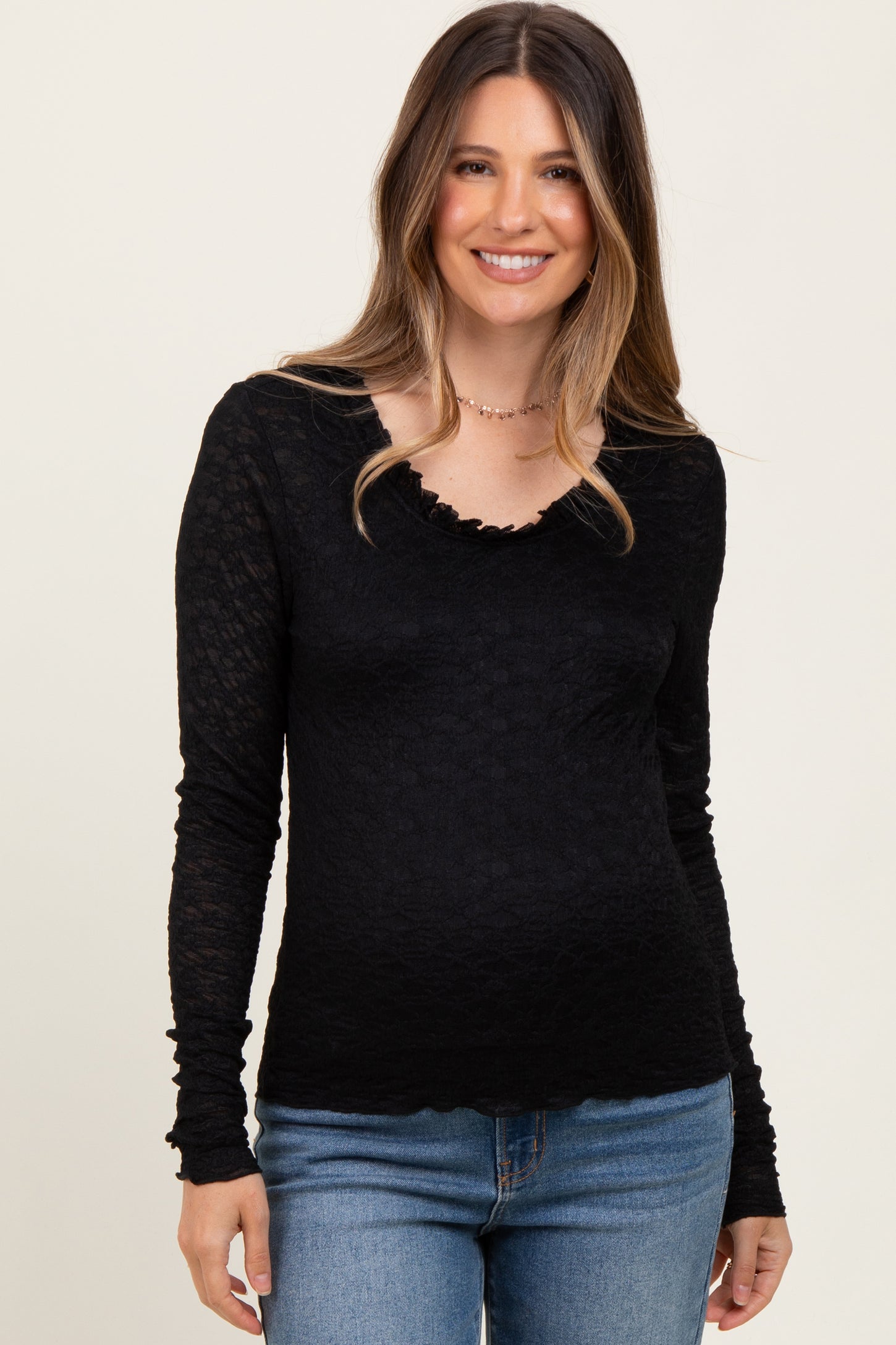 woman wearing a black long sleeve maternity top with a scalloped neckline and visible baby bump