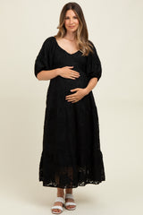 woman wearing a black lace maternity dress with puff sleeves and holding her baby bump