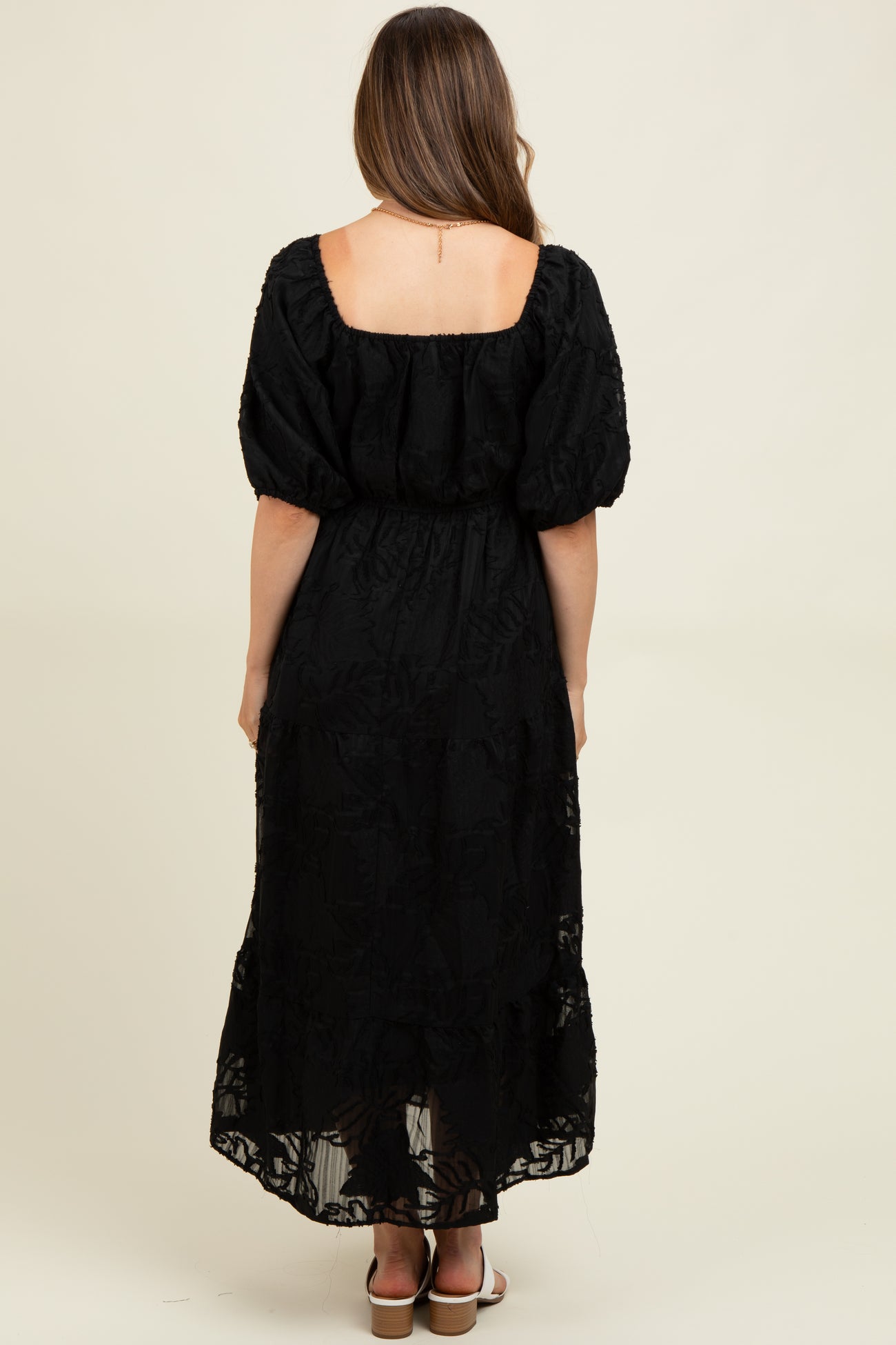 woman wearing a black maxi maternity dress with puff sleeves and a floral pattern, seen from the back