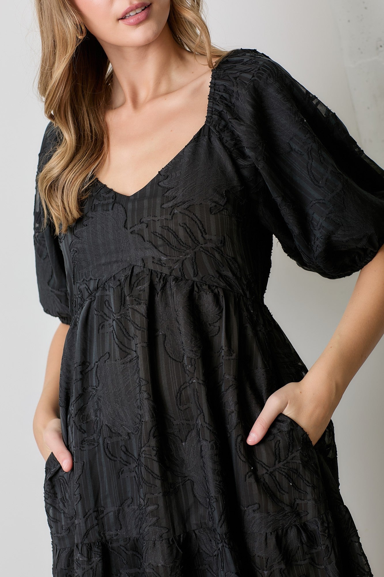 woman wearing a black puff sleeve dress with floral texture and pockets
