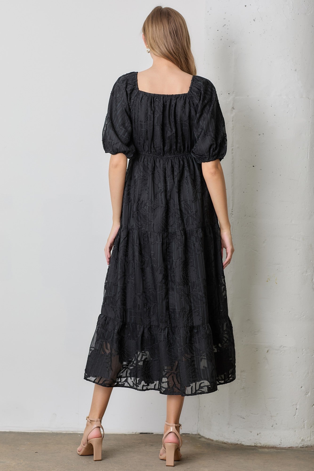 woman wearing a black puff sleeve midi dress with a square neckline and tiered hem, shown from the back