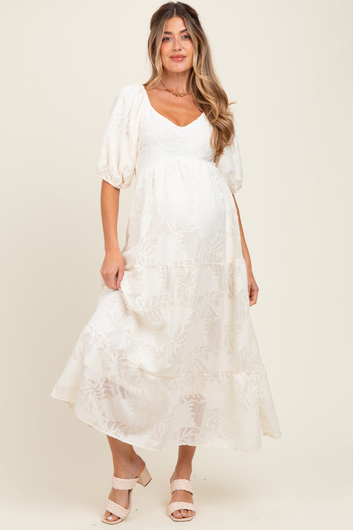 woman wearing a cream floral print maternity maxi dress with puff sleeves and a visible baby bump