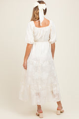 woman wearing a cream maternity maxi dress with puff sleeves and a tiered skirt, styled with a hair ribbon