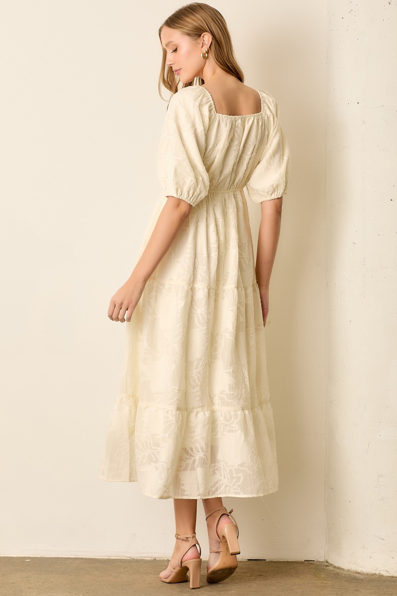 woman wearing a cream colored puff sleeve maxi dress with a square neckline and tiered skirt