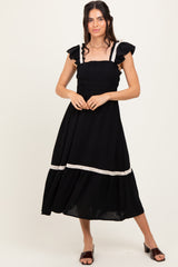 woman wearing a black maxi dress with ruffled sleeves and a smocked bodice, standing with hands on her hips