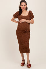 woman wearing a brown textured maternity dress with short puff sleeves and holding her baby bump