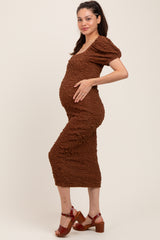 woman wearing a brown textured maternity dress and holding her baby bump