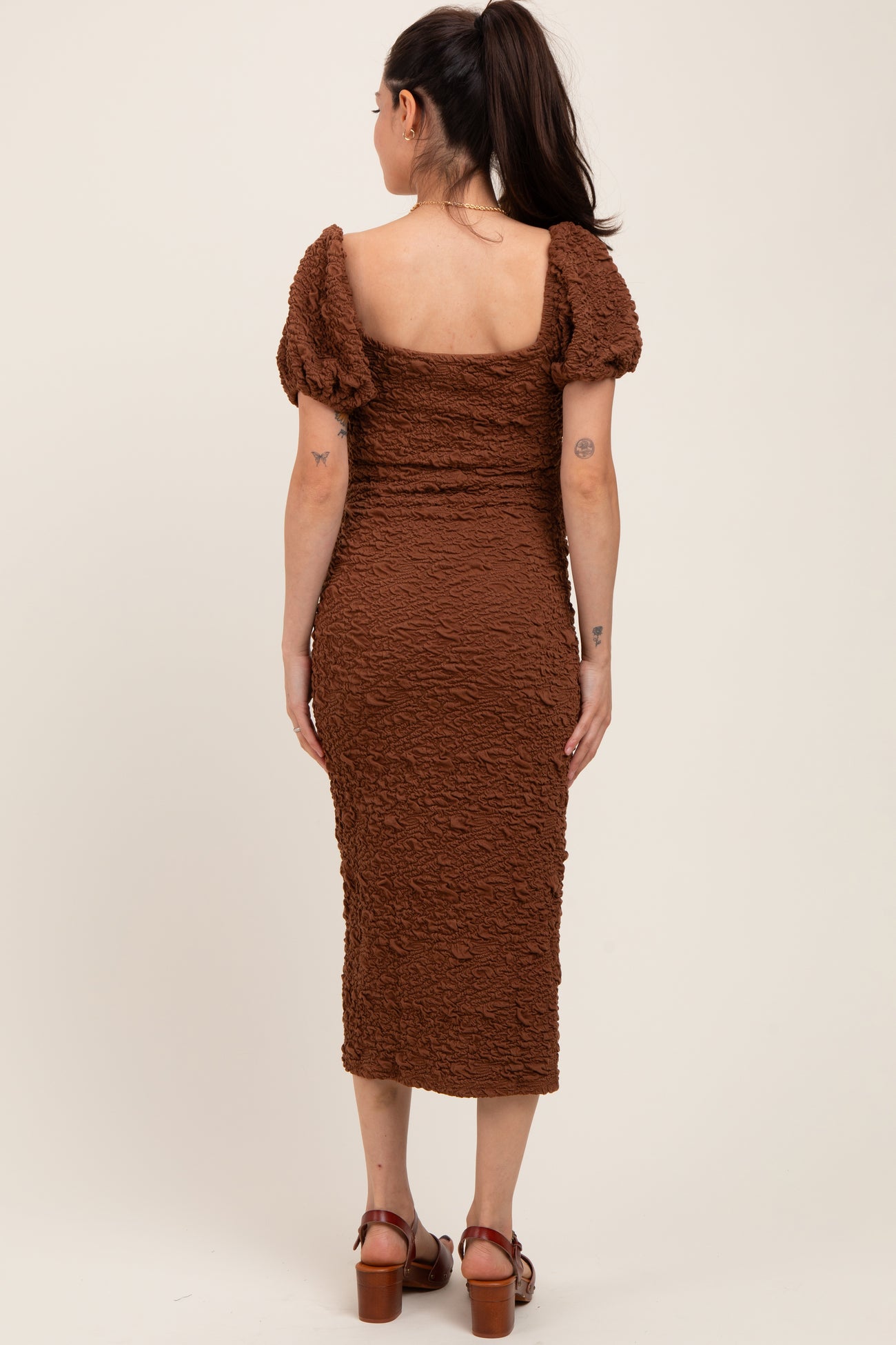 woman wearing a brown textured maternity dress with puff sleeves and a fitted silhouette, showing her back