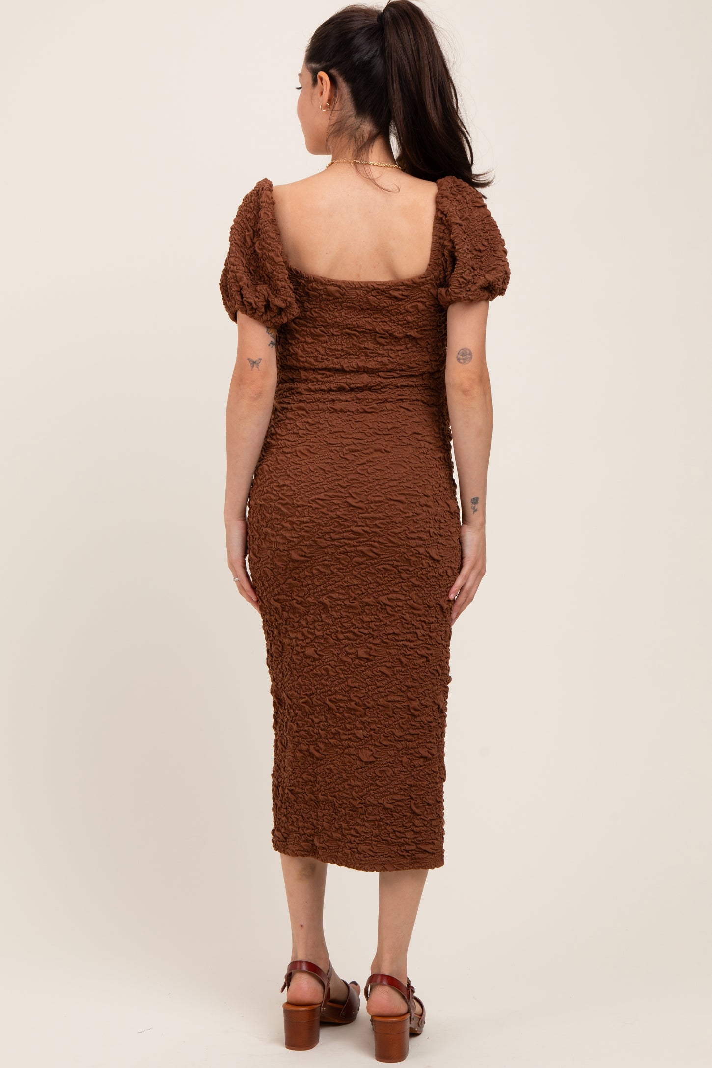 woman wearing a brown textured maternity dress with puff sleeves and a fitted silhouette, showing her back