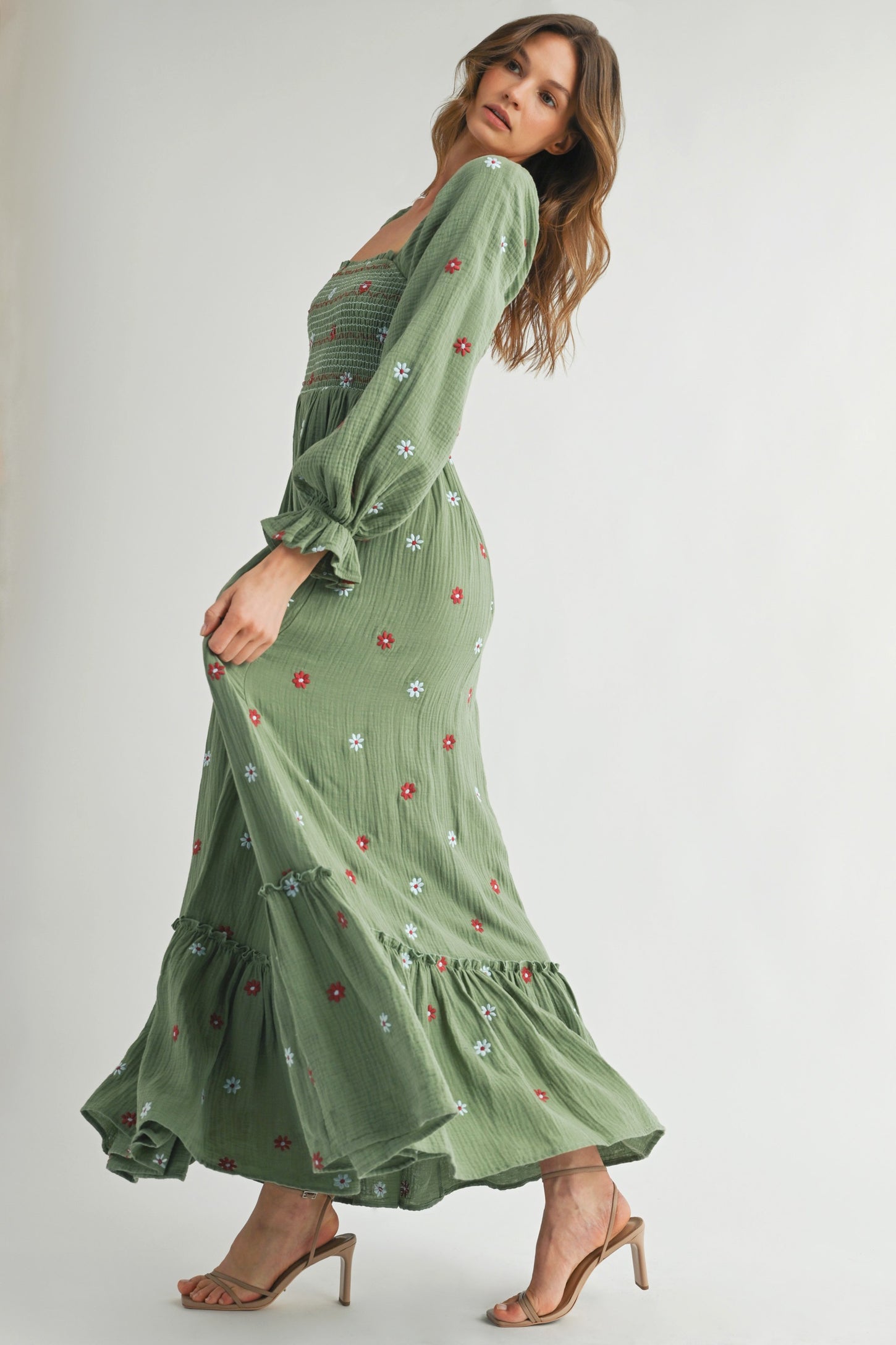 woman wearing a green maxi dress with floral embroidery and puff sleeves, standing in a side pose with heels on
