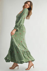 woman wearing a green maxi dress with floral embroidery and puff sleeves, standing in a side pose with heels on