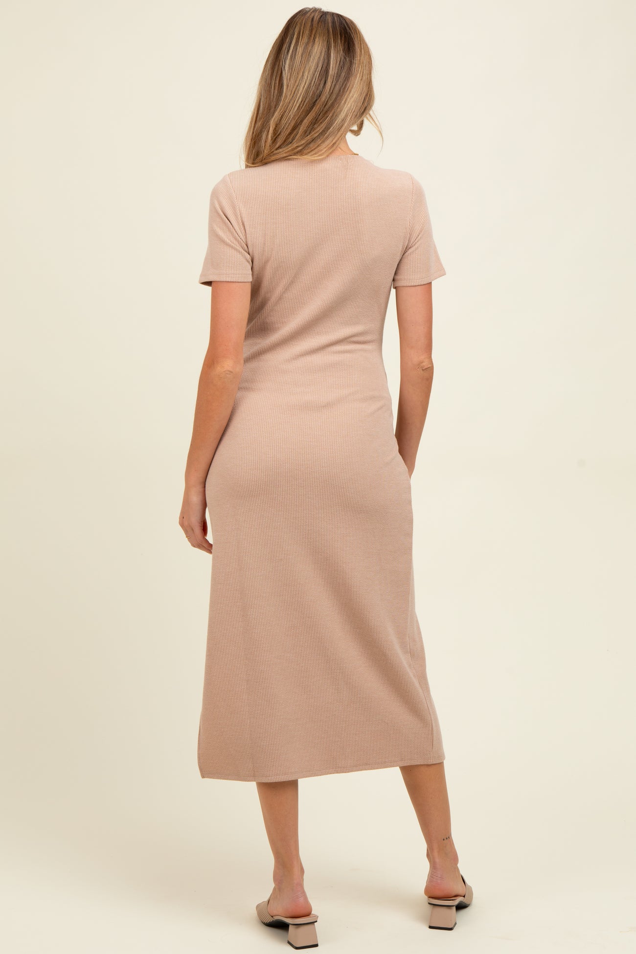 woman wearing a beige ribbed maternity dress with short sleeves and a midi length, showing a side view
