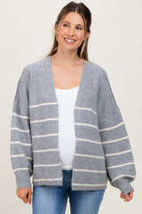 woman wearing a gray striped maternity cardigan over a white top and blue jeans, showing her baby bump