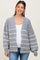 woman wearing a gray striped maternity cardigan over a white top and blue jeans, showing her baby bump