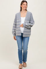 woman wearing a gray and white striped maternity cardigan and holding her baby bump with blue jeans and flats