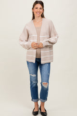 woman wearing a beige striped maternity cardigan over a brown top and blue distressed jeans, smiling at the camera