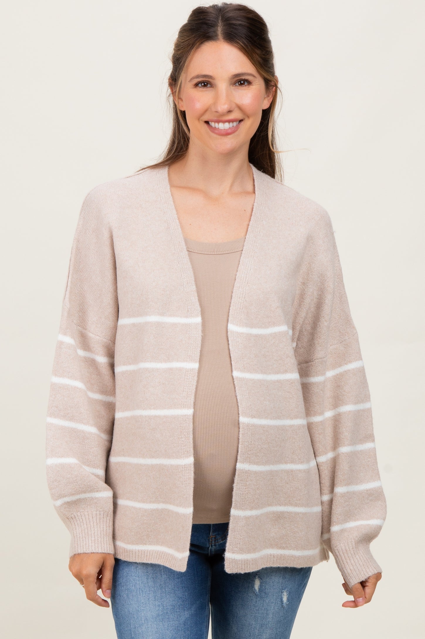 woman wearing a beige and white striped maternity cardigan over a fitted top and showing her baby bump