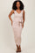 woman wearing a light pink ribbed midi dress with a v-neck and a tie belt, standing and smiling
