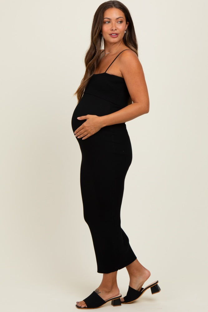 woman wearing a black ribbed maternity dress, holding her baby bump, standing in profile with sandals on