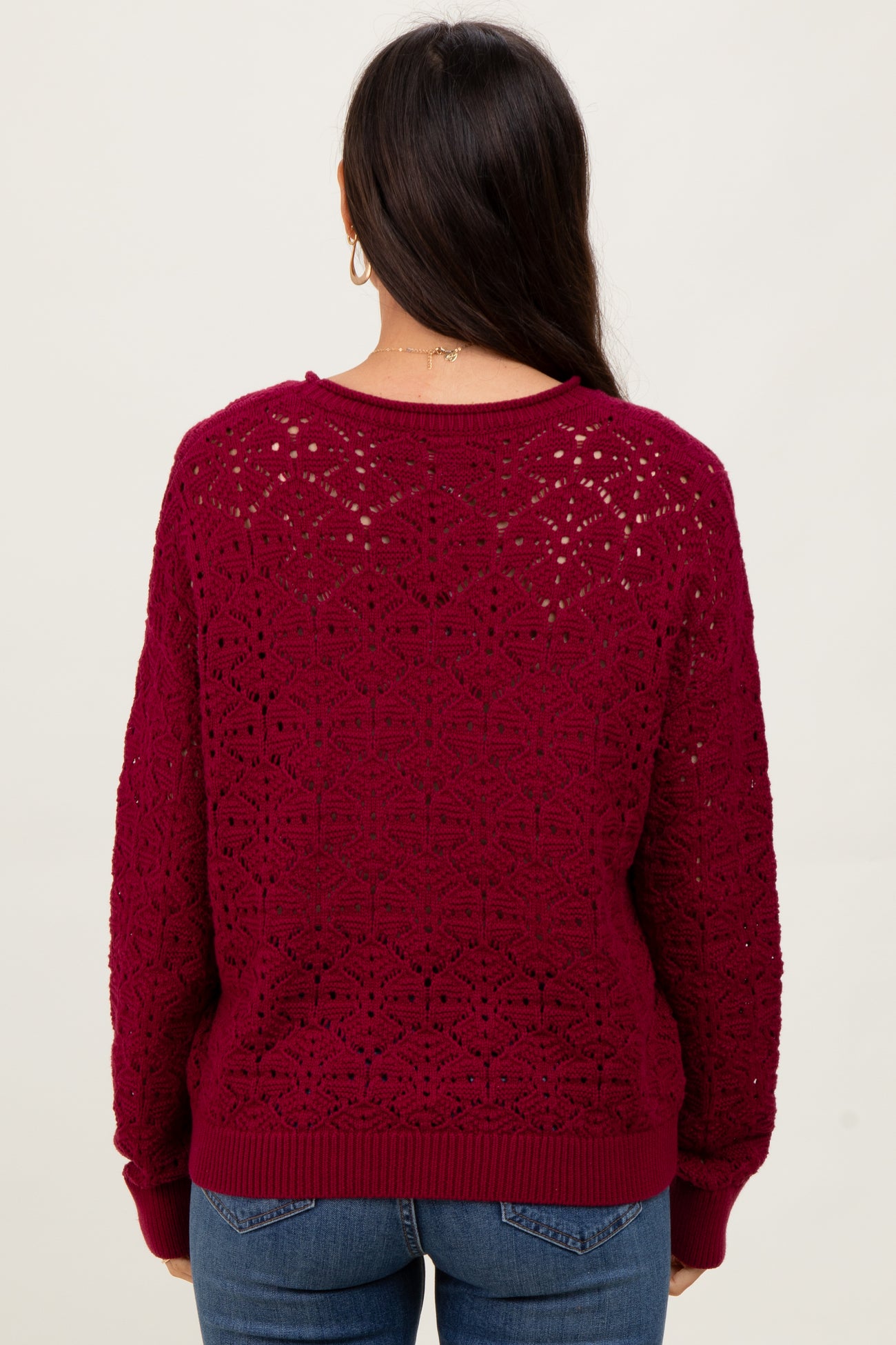 woman wearing a burgundy crochet knit sweater with a relaxed fit, viewed from the back