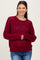 woman wearing a burgundy maternity sweater with a lace pattern and long sleeves, smiling and standing with hands together